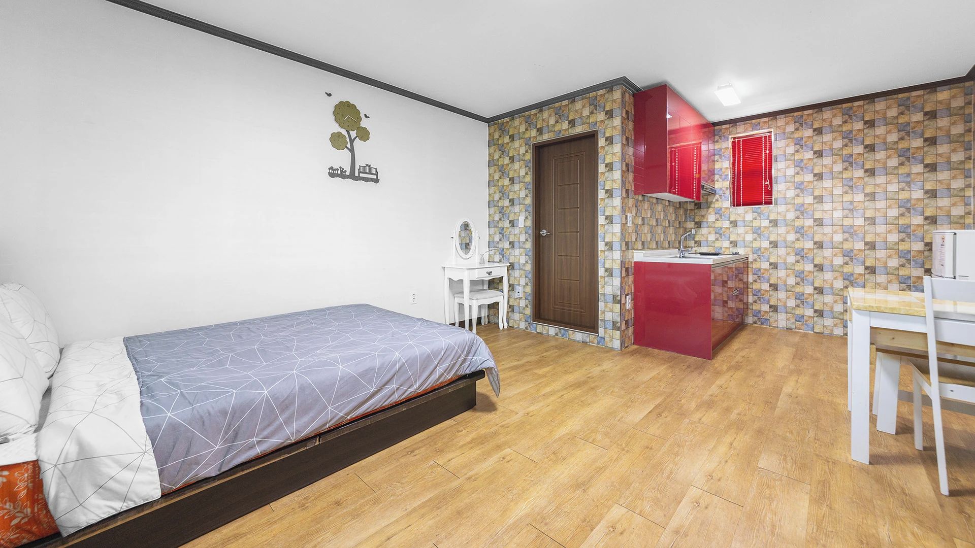 Een slaapkamer met een bed, een klein bureau en een kitchenette met een rode kast.