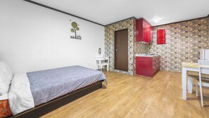 Ein Schlafzimmer mit einem Bett, einem kleinen Schreibtisch und einer Küchenzeile mit einem roten Schrank.