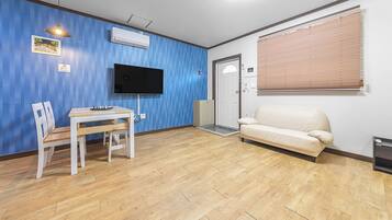 A room with a wooden floor, a white sofa, a TV mounted on the wall, and a door with a window.