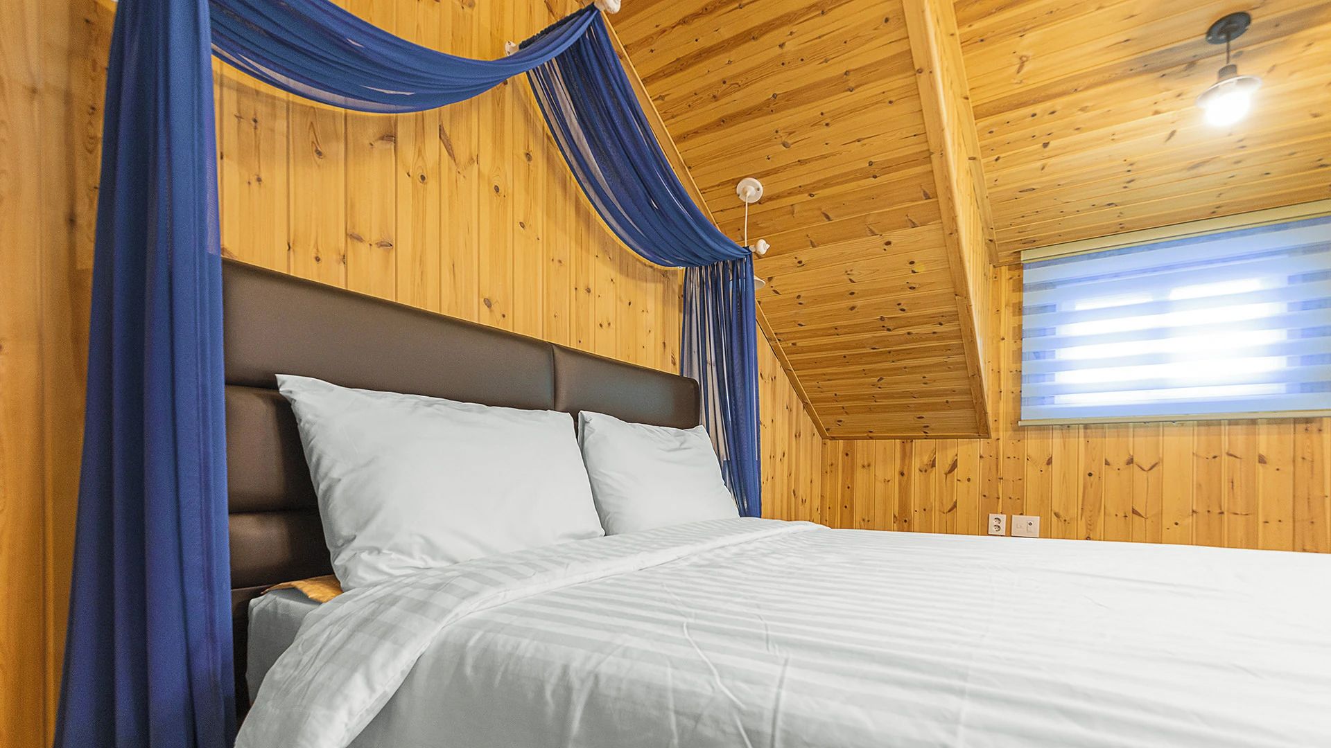 Un dormitorio con techo de madera, cama con ropa de cama blanca y cortinas azules.