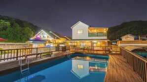 A swimming pool with a wooden deck, a two-story building with a balcony, and a night sky with stars. - Gapyeong Etoile Pension (Gapyeong)