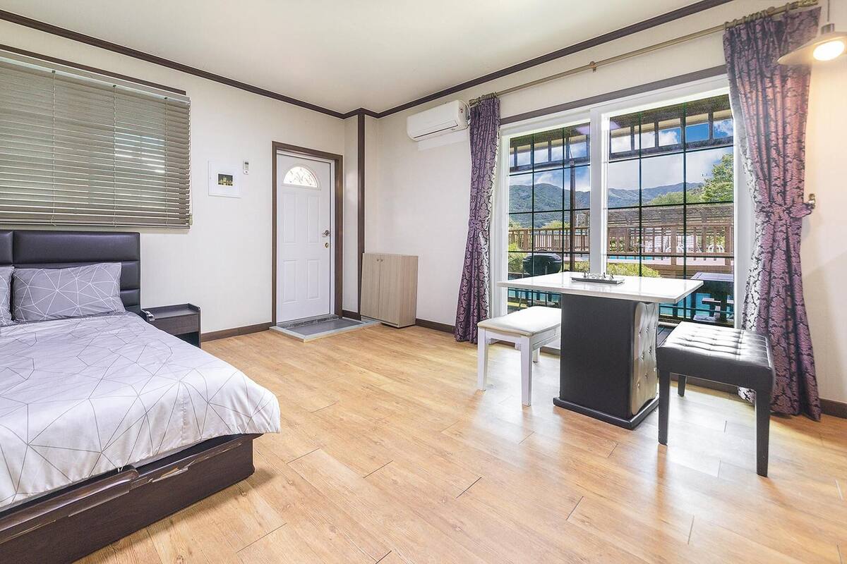 A bedroom with a bed, a desk, and a view of the outdoors.