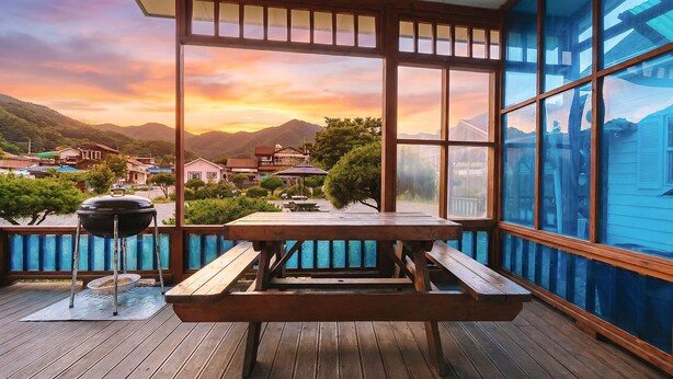 A wooden deck with a picnic table and grill, overlooking a scenic village and mountains. - Gapyeong Etoile Pension (Gapyeong)