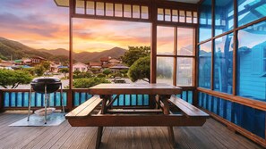 Une terrasse en bois avec une table de pique-nique et un barbecue, offrant une vue panoramique sur un village pittoresque et les montagnes.