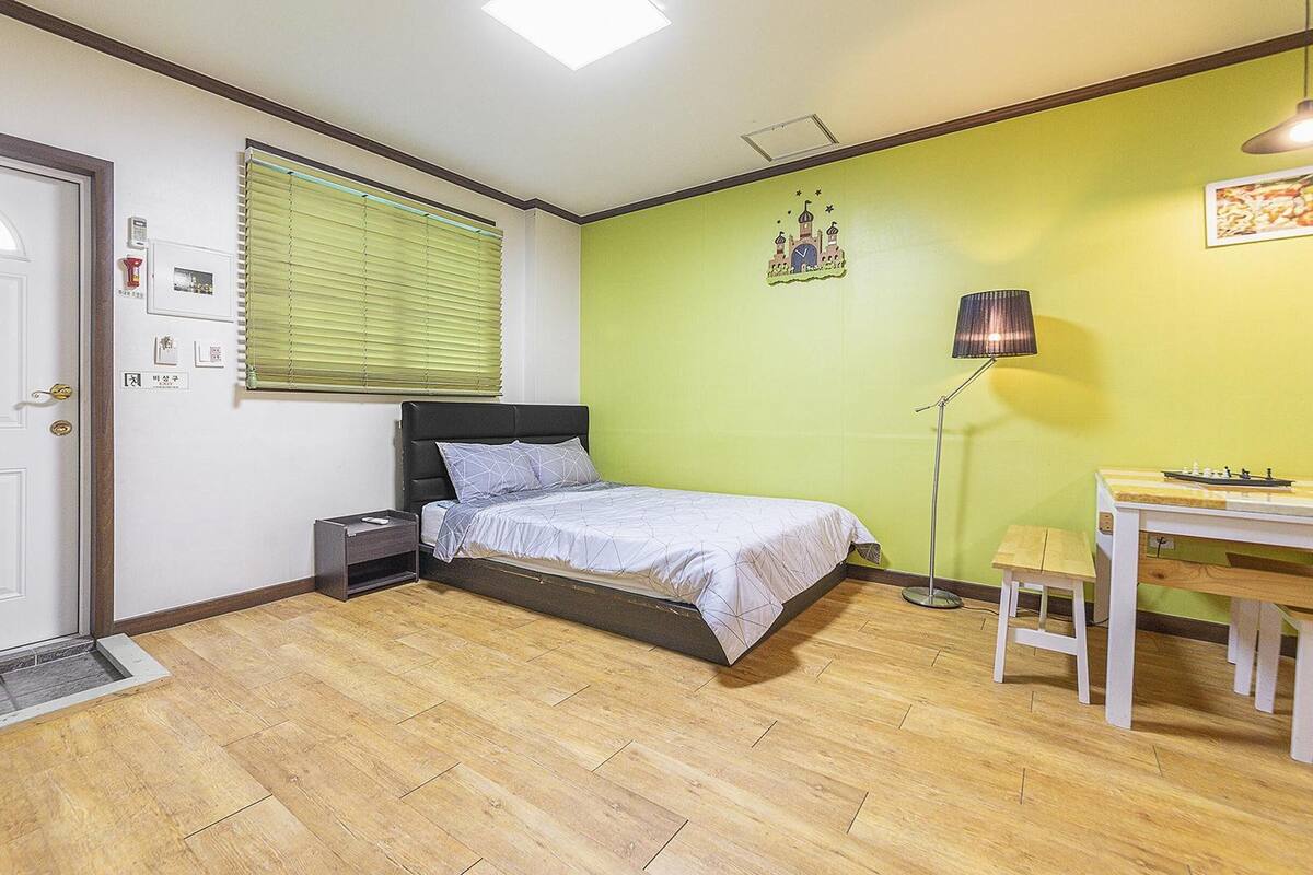 A bedroom with a bed, bedside table, lamp, and a small desk with a chair.