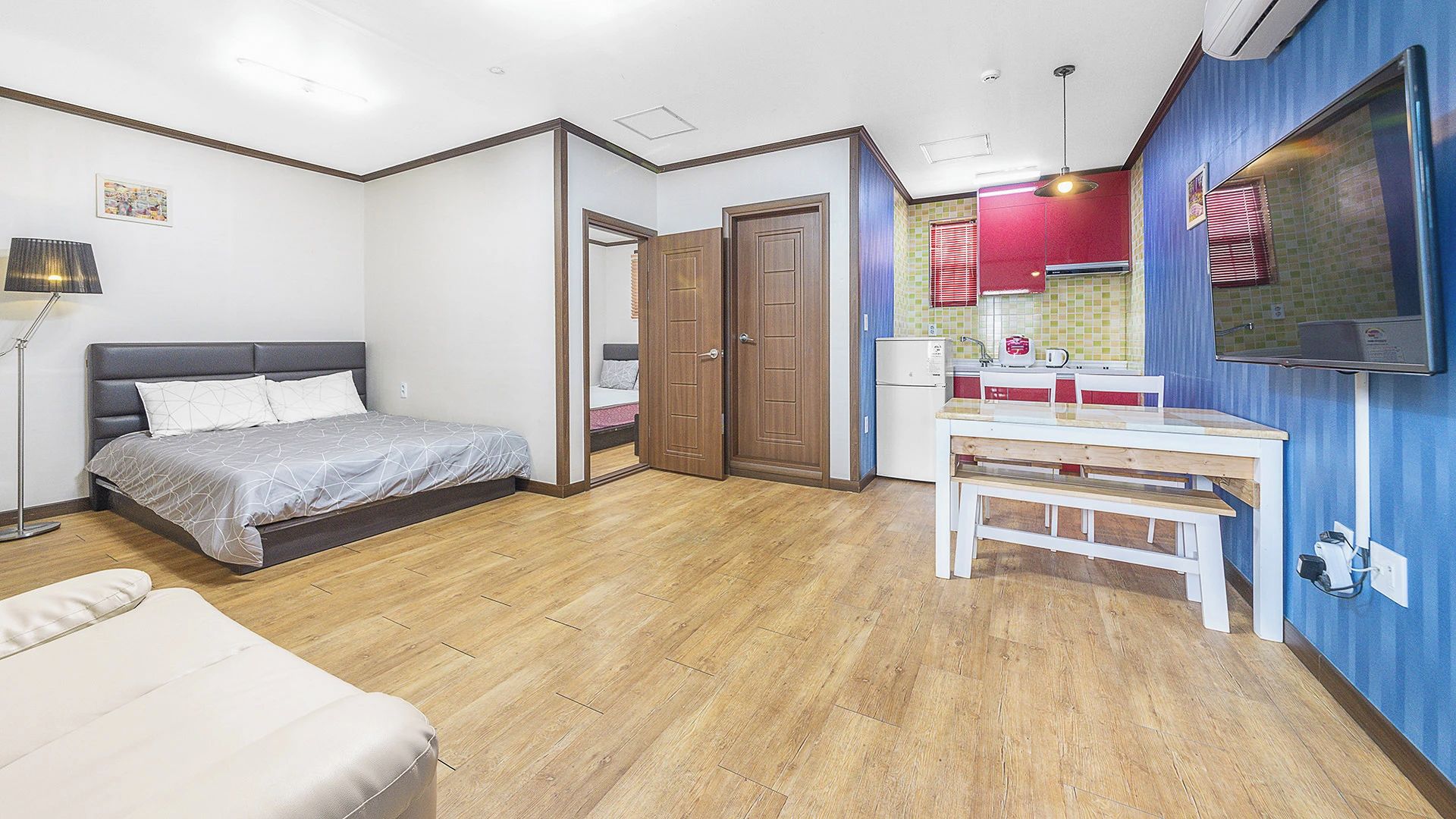 Een slaapkamer met een bed, nachtkastje en een bureau met stoel. Een deur leidt naar een andere kamer.