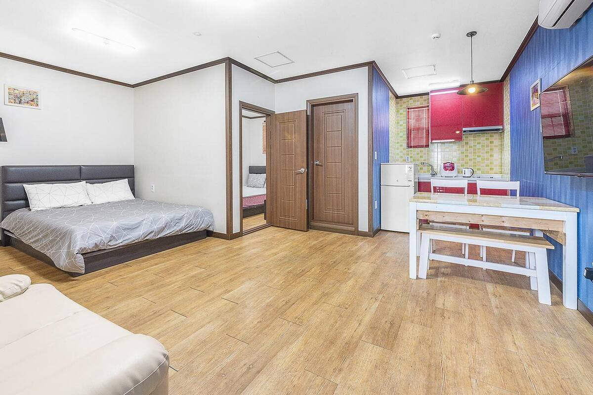 A bedroom with a bed, bedside table, and a small kitchenette with a refrigerator and microwave.