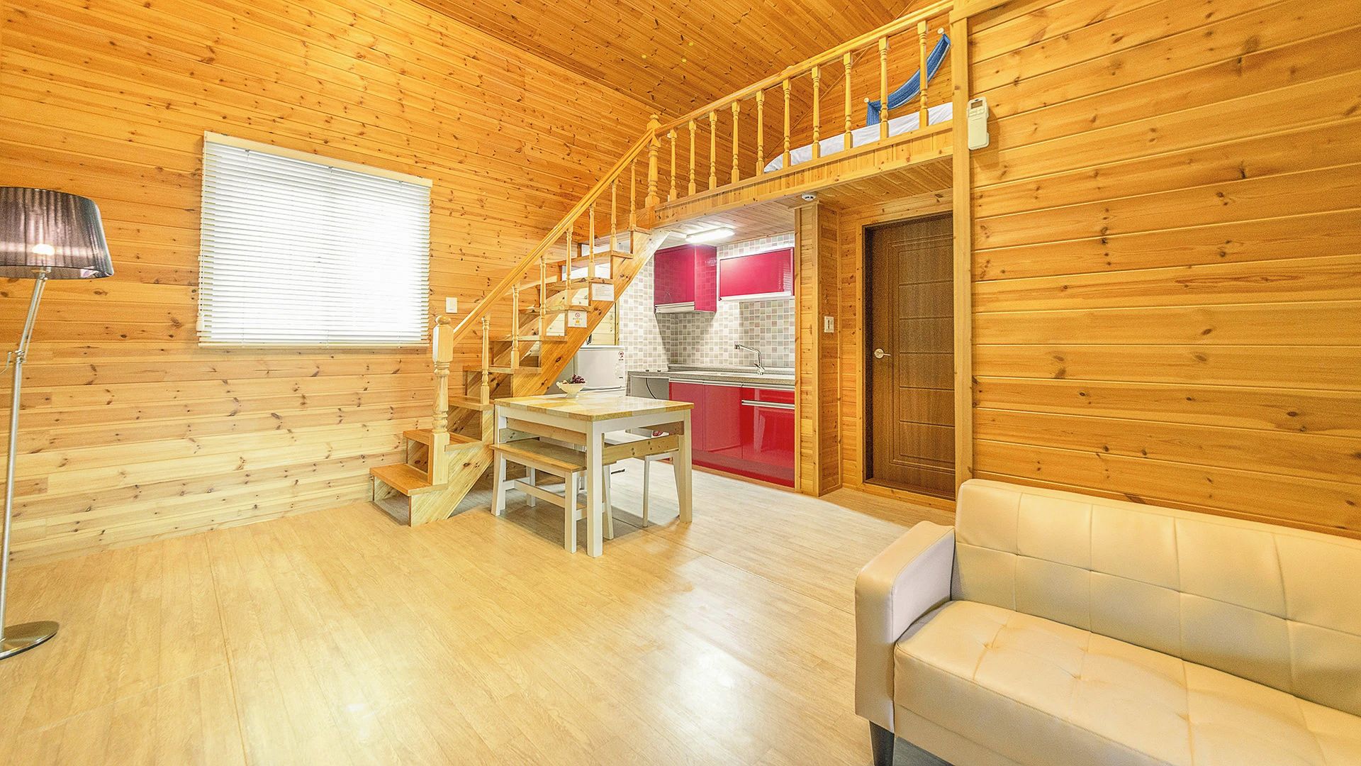 A wooden interior with a staircase leading to a kitchen area, a dining table, and a sofa.