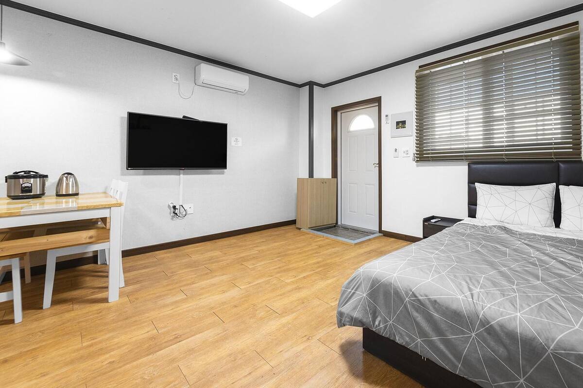 A modern bedroom with a bed, a TV, a desk, and a door.