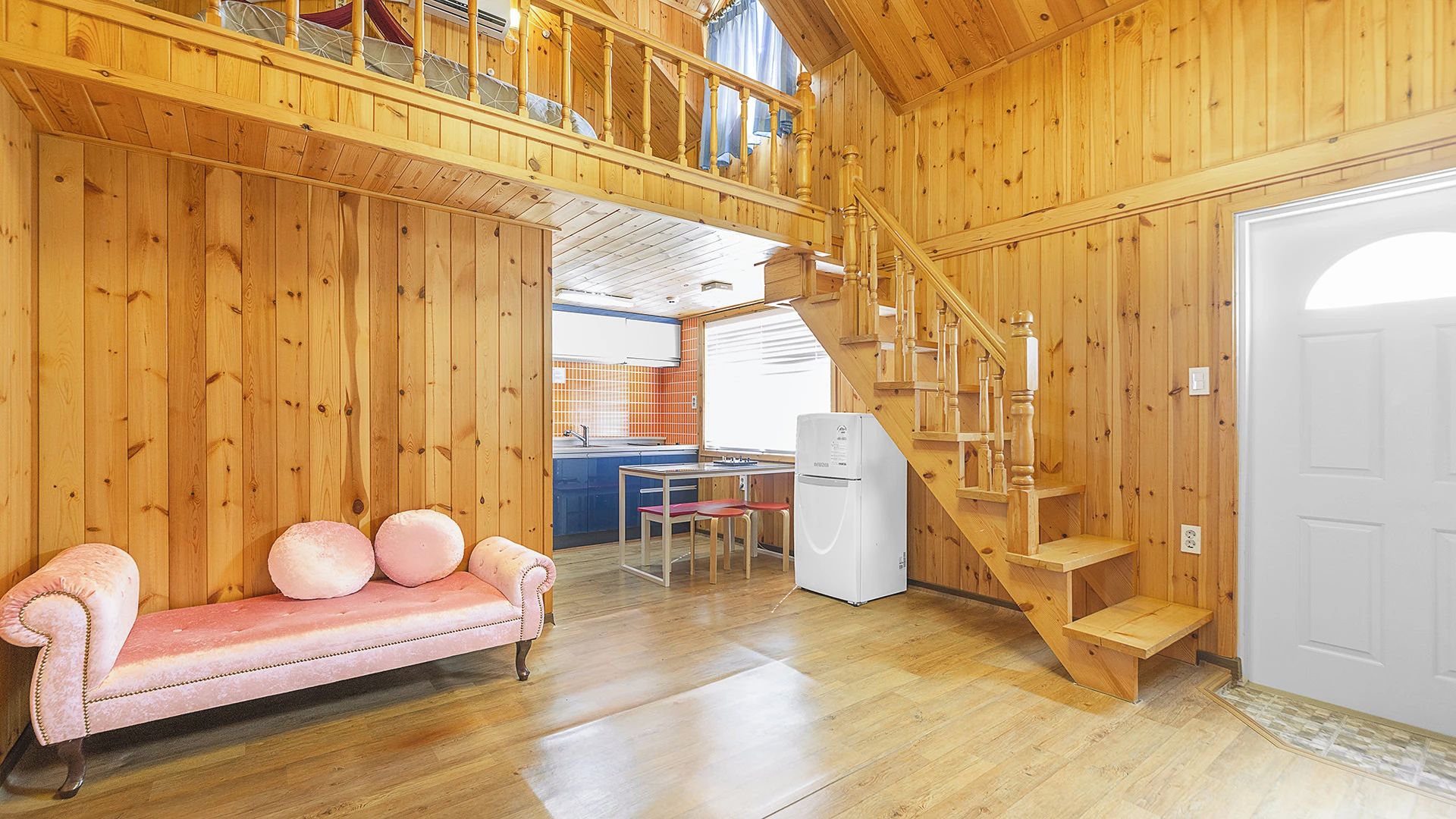 A wooden interior with a sofa, a staircase, and a kitchen area.