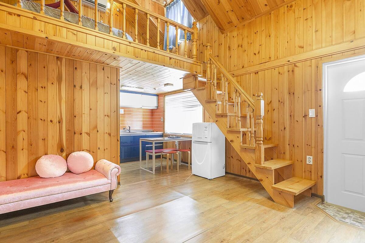 A cozy cabin interior with a wooden staircase, a dining area, and a sofa with cushions.