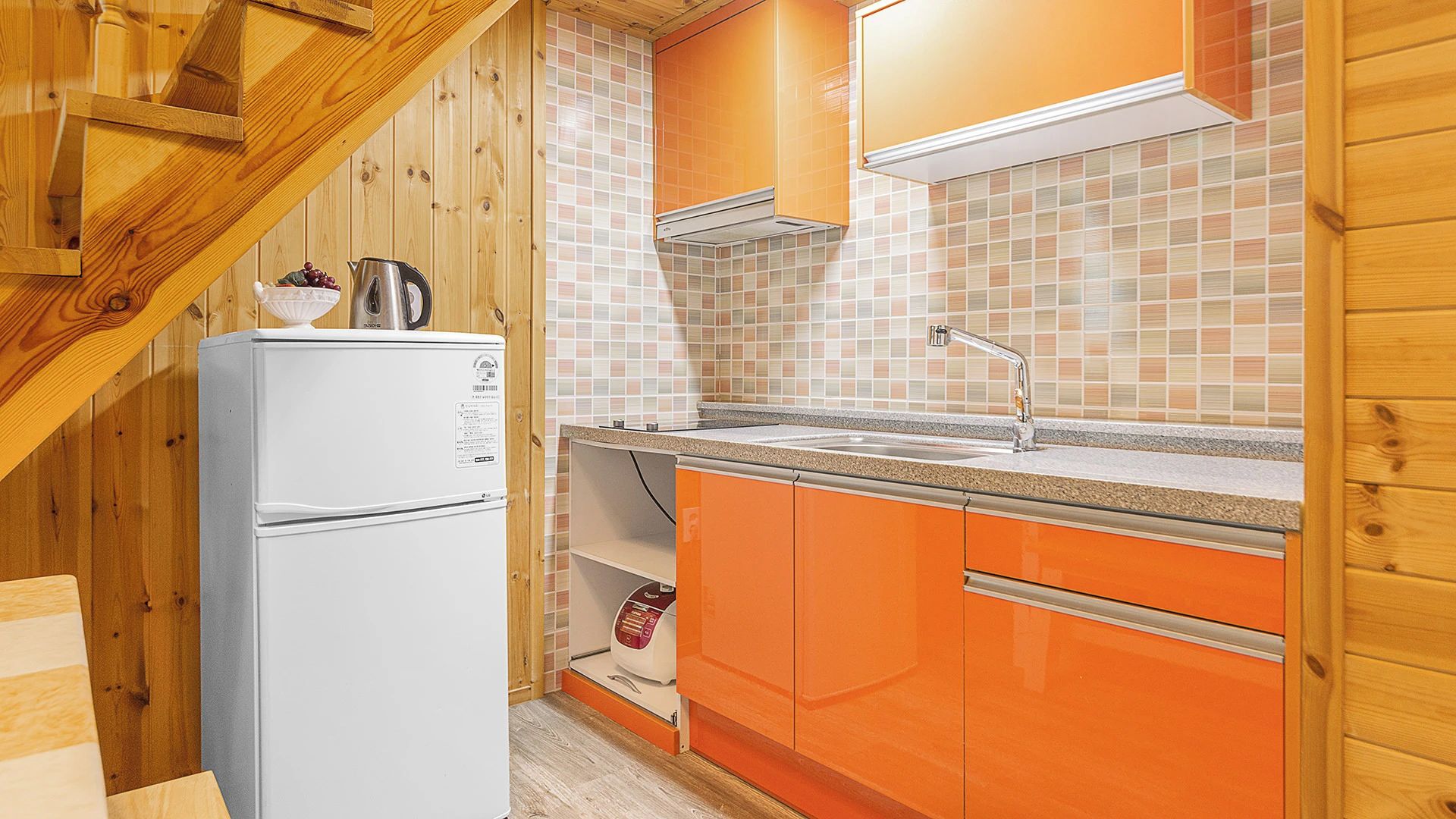 Een keuken met houten wanden, een witte koelkast, oranje kastjes en een betegelde achterwand.