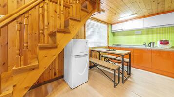 A wooden staircase leading to a kitchen with a white refrigerator, a wooden table, and a green tiled backsplash.