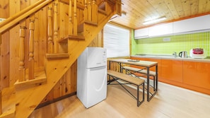 Een houten trap leidt naar een keuken met een witte koelkast, een houten tafel en een groene betegelde achterwand.