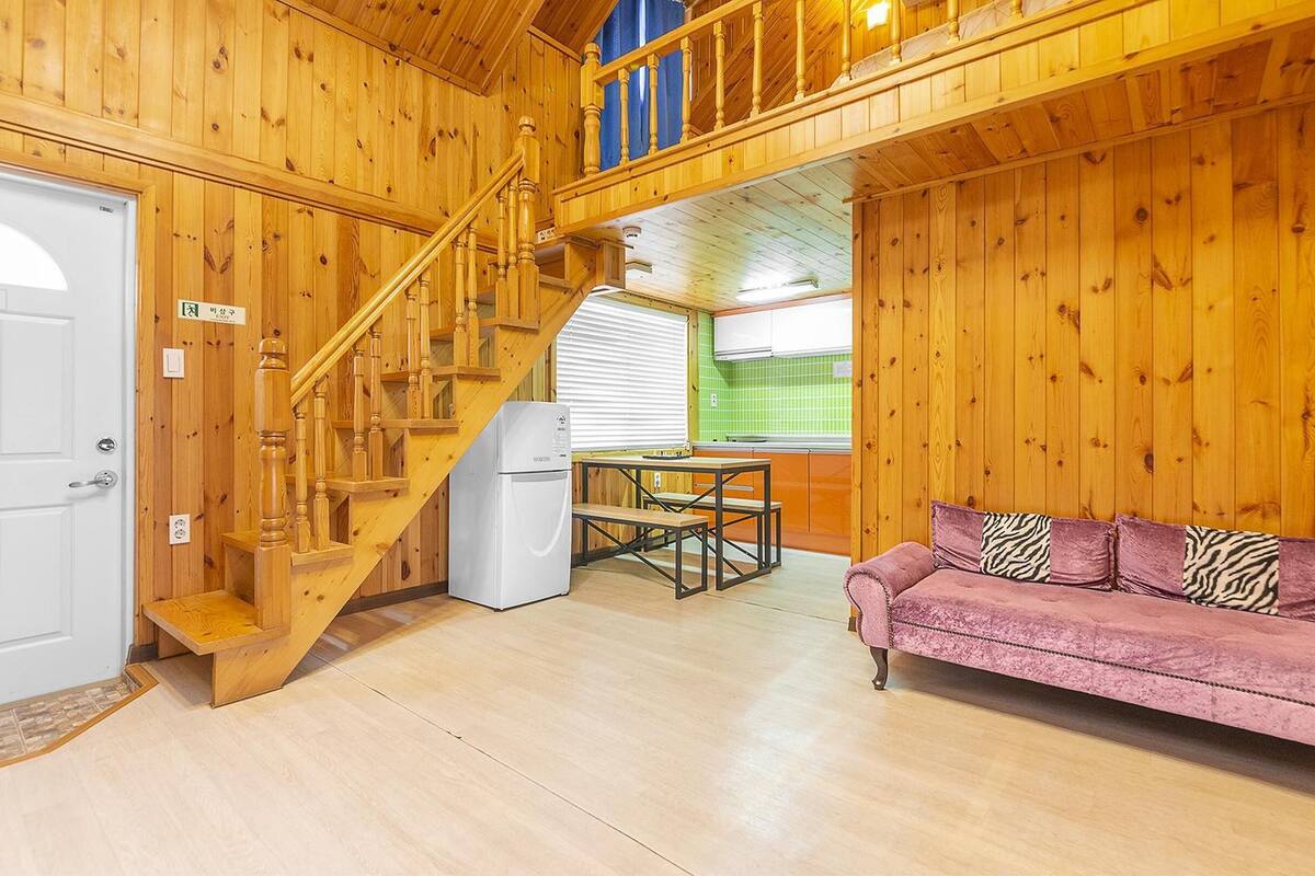 A wooden interior with a staircase, a sofa, and a kitchen area.