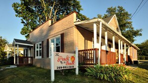 Une maison à deux étages avec un porche, une enseigne indiquant « The Peach by the Beach », et un numéro de téléphone.
