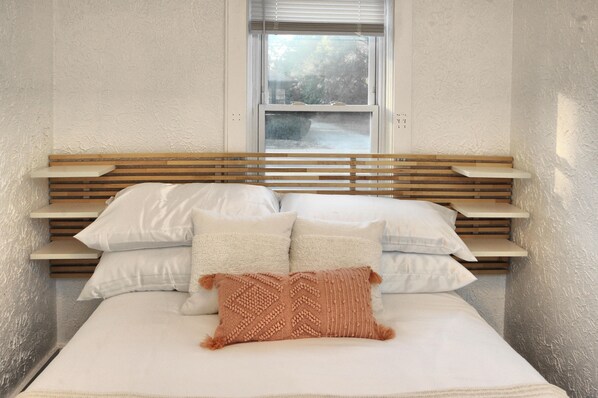 Una cama con cabecera de madera, ropa de cama blanca y una ventana arriba.