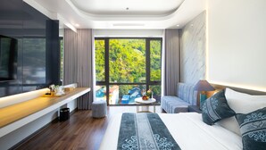 A modern hotel room with a large bed, a TV, a wooden bench, and a view of greenery outside. - Glenda Tower Moc Chau Hotel (Moc Chau)