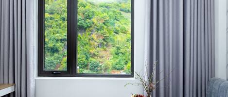 A room with a large window, a bed, a bedside table with a vase of flowers, and a grey sofa.