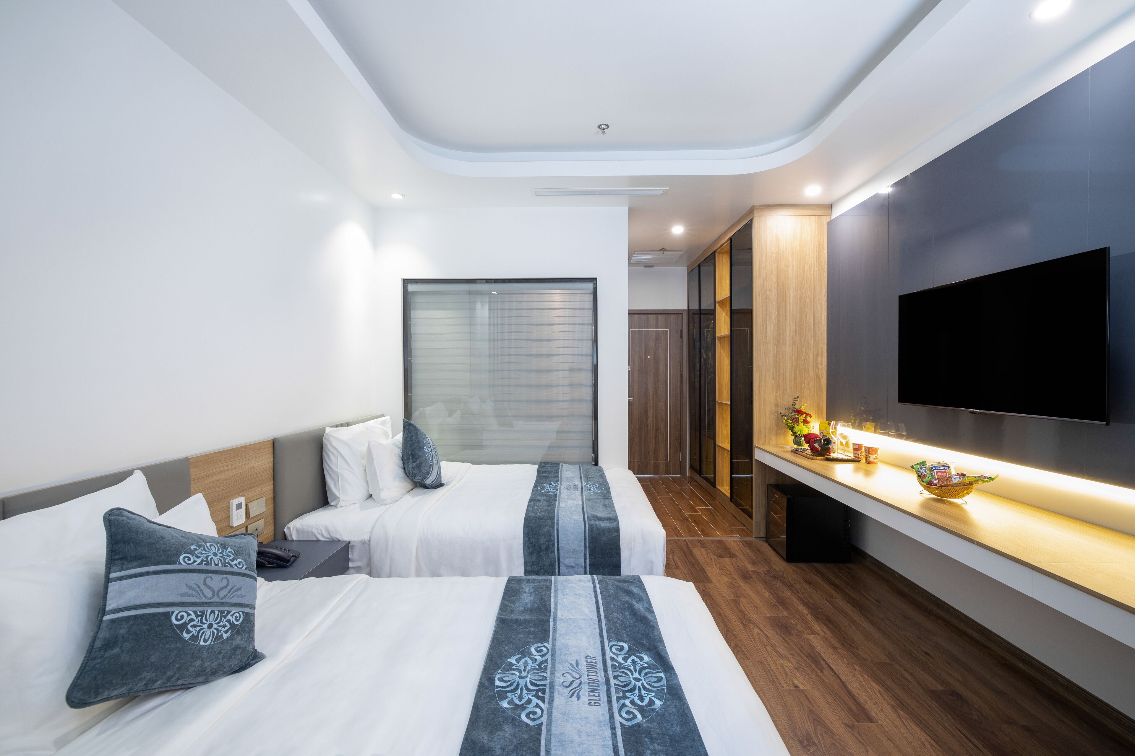 Una habitación de hotel moderna con dos camas, un televisor de pantalla plana, un tocador de madera y un ventanal grande.