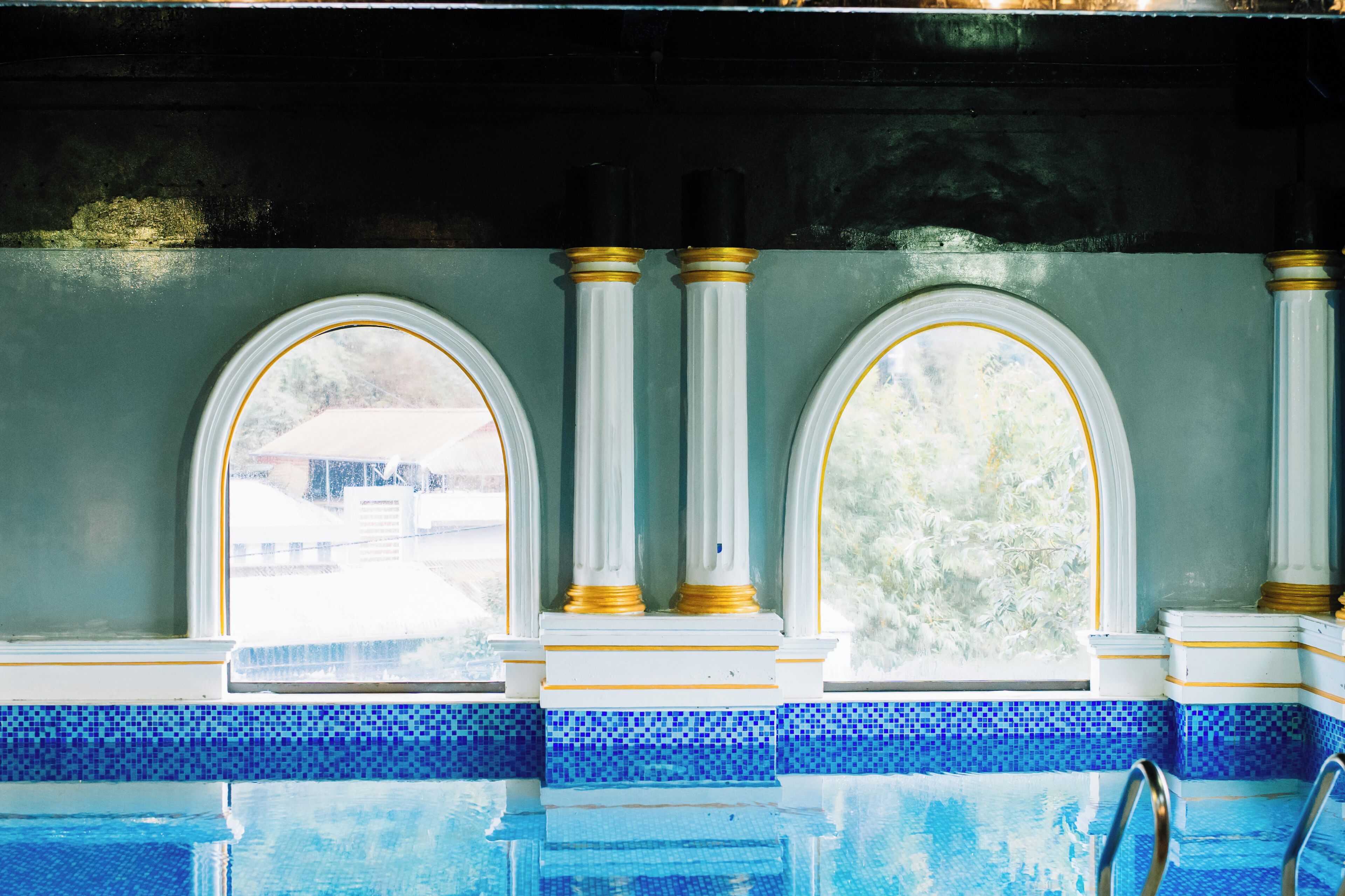 A swimming pool with a tiled edge and a view through arched windows.