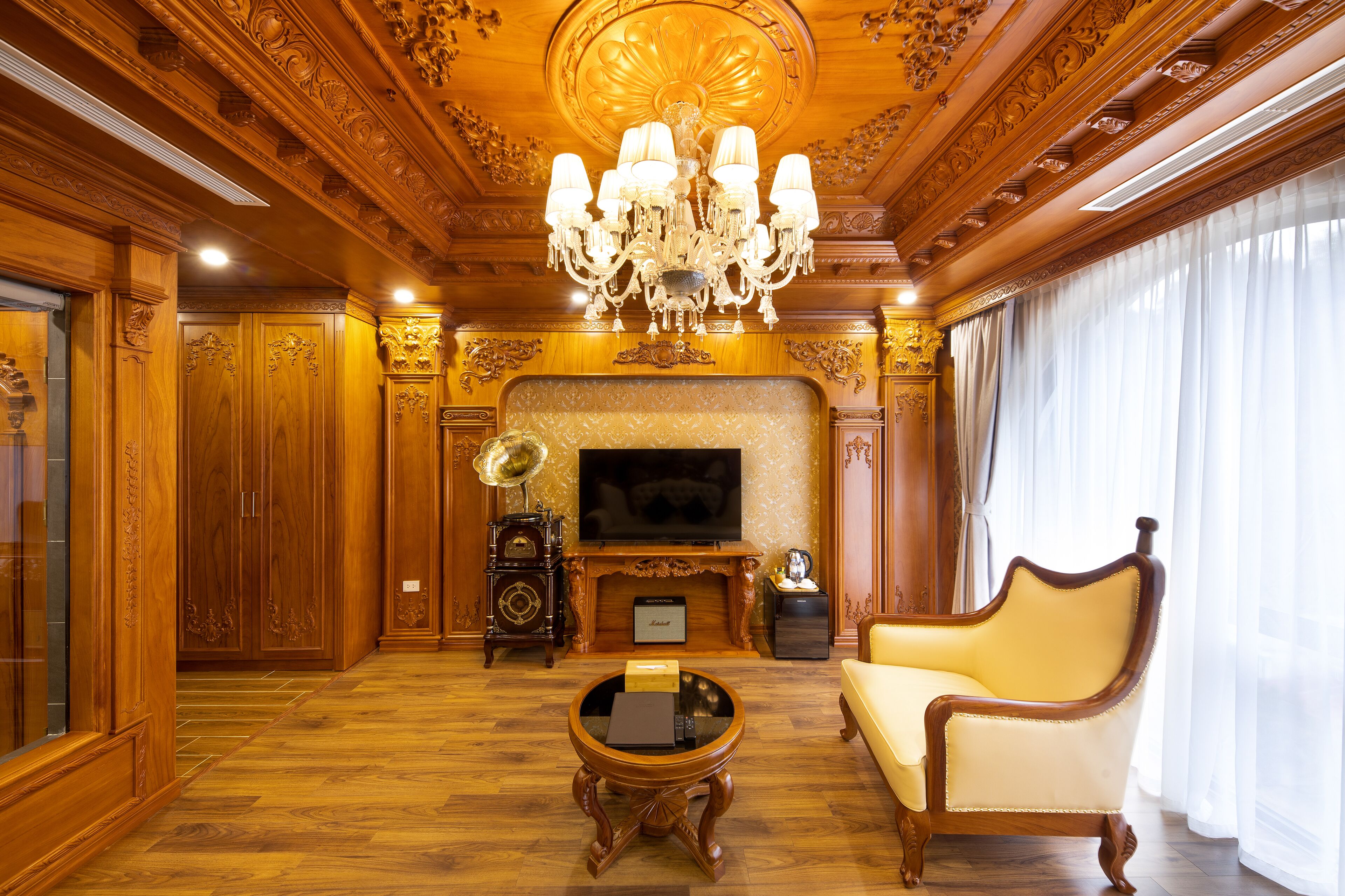 A luxurious living room with a large chandelier, a television, and a classic armchair.