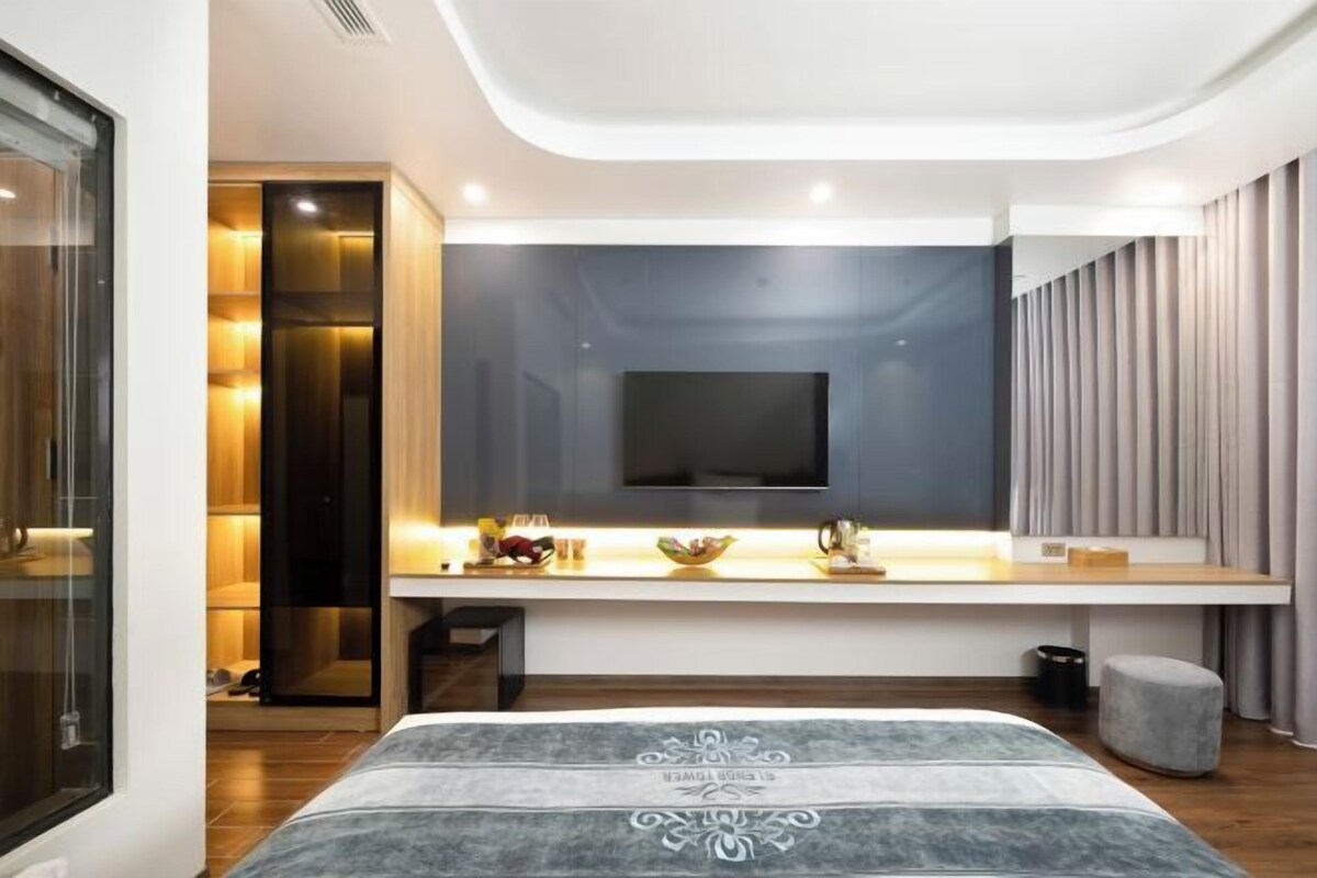 Un dormitorio moderno con una cama grande, un televisor montado en la pared, una mesita de noche con un cuenco y un taburete pequeño.