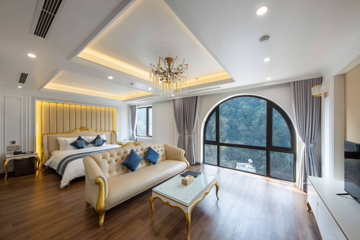 A spacious bedroom with a large bed, a sofa, a glass coffee table, and a TV.