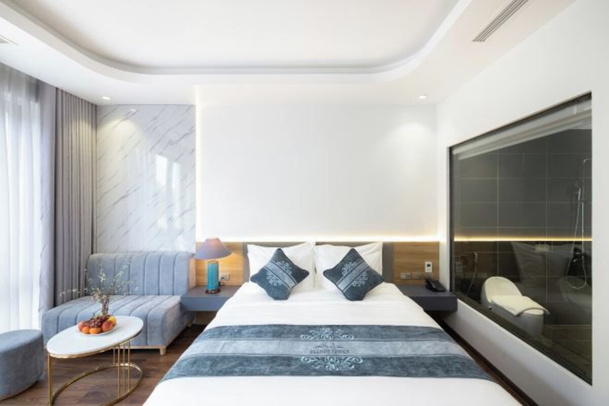 A modern hotel room with a large bed, a seating area, and a large window.
