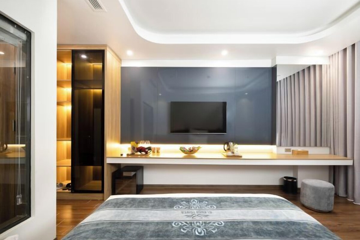 Un dormitorio moderno con cama, mesita de noche, televisor y una pequeña zona de estar.