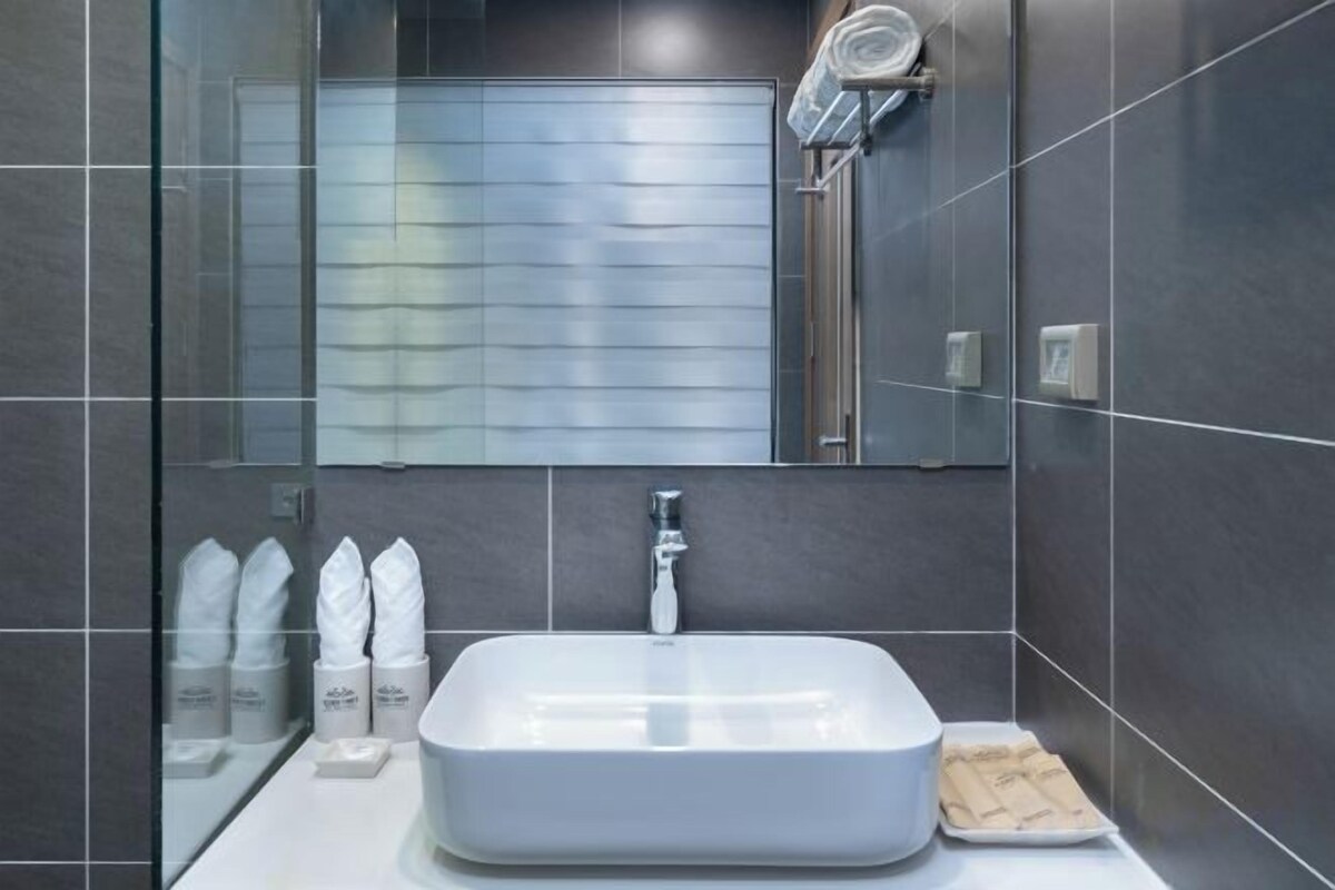 Un baño moderno con un lavamanos rectangular, un espejo encima y una zona de ducha a la vista al fondo.