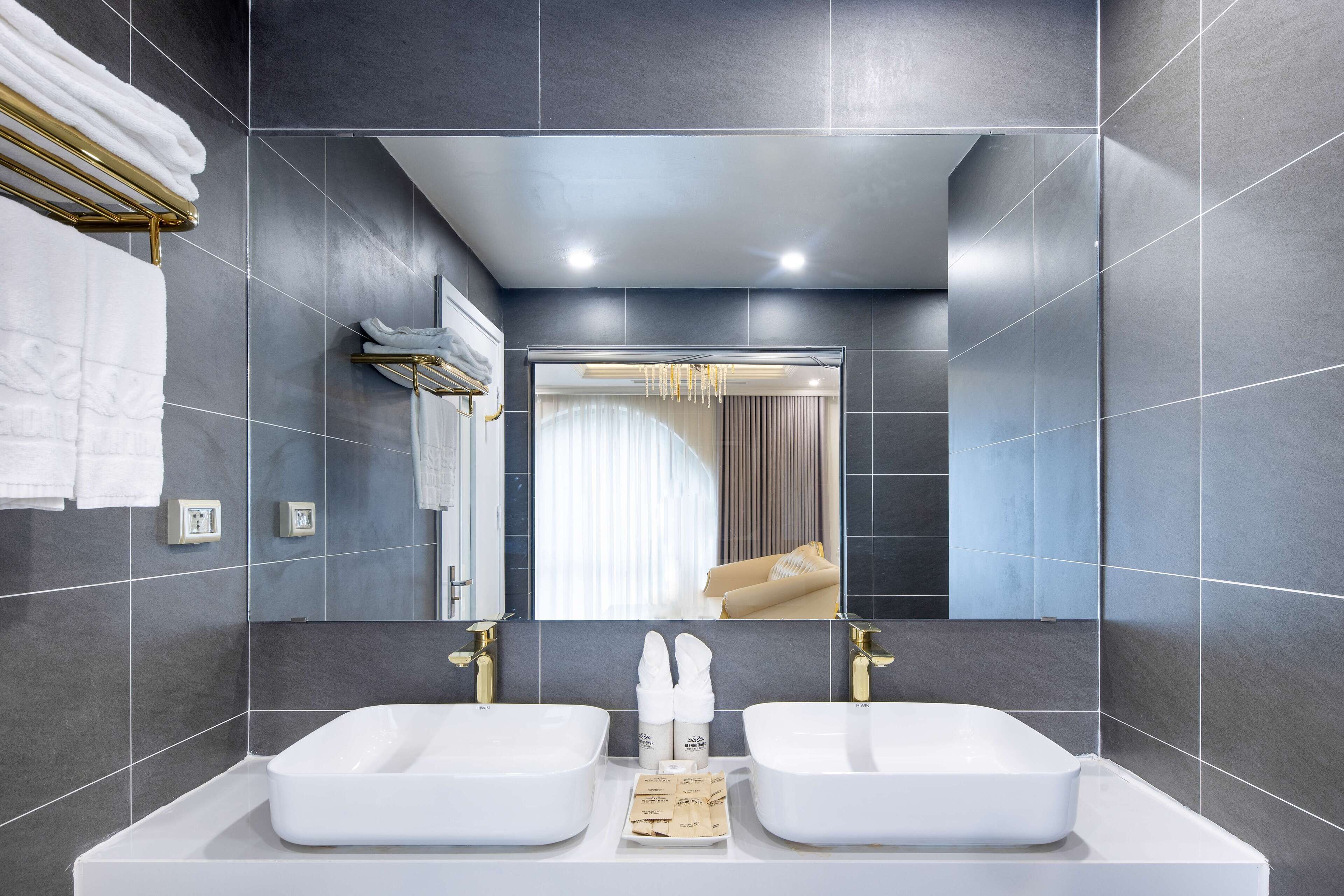 A modern bathroom with two sinks, dark tiled walls, and a large mirror.