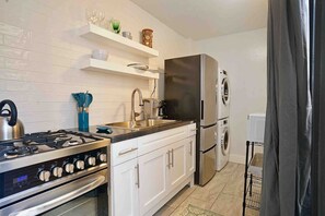 A modern kitchen with white cabinets, stainless steel appliances, and a built-in oven. - Ocean View Studio • by Magen's • Pool & Generator (Northside)