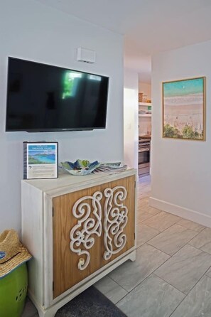 A room with a flat-screen TV mounted on the wall, a wooden cabinet with decorative carvings, a framed welcome sign, and a framed landscape painting.