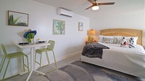 A bedroom with a bed, two chairs, a desk, and a ceiling fan. - Ocean View Studio • by Magen's • Pool & Generator (Northside)