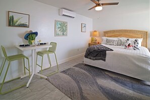 A bedroom with a bed, two chairs, a desk, and a ceiling fan. - Ocean View Studio • by Magen's • Pool & Generator (Northside)