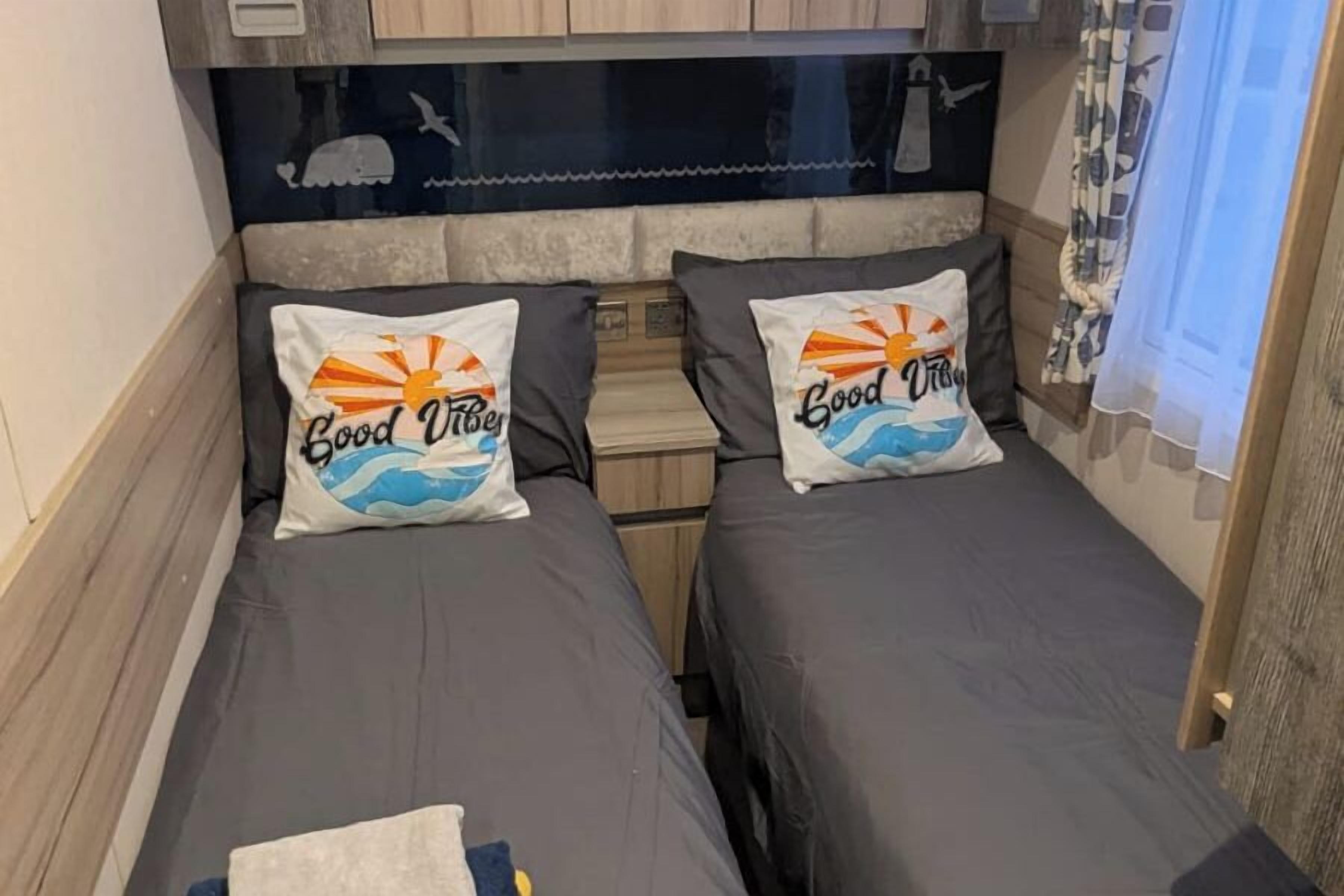 Una habitación pequeña y acogedora con dos camas individuales, cada una con un cojín con diseño de sol y olas.
