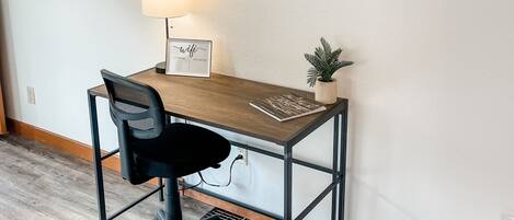 Un espace de travail aménagé à la maison, avec un bureau, une chaise, une lampe et un panneau décoratif avec le mot « MAISON » accroché au mur.