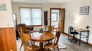 Un coin repas avec une table et des chaises en bois, un canapé et un petit bureau avec une lampe.