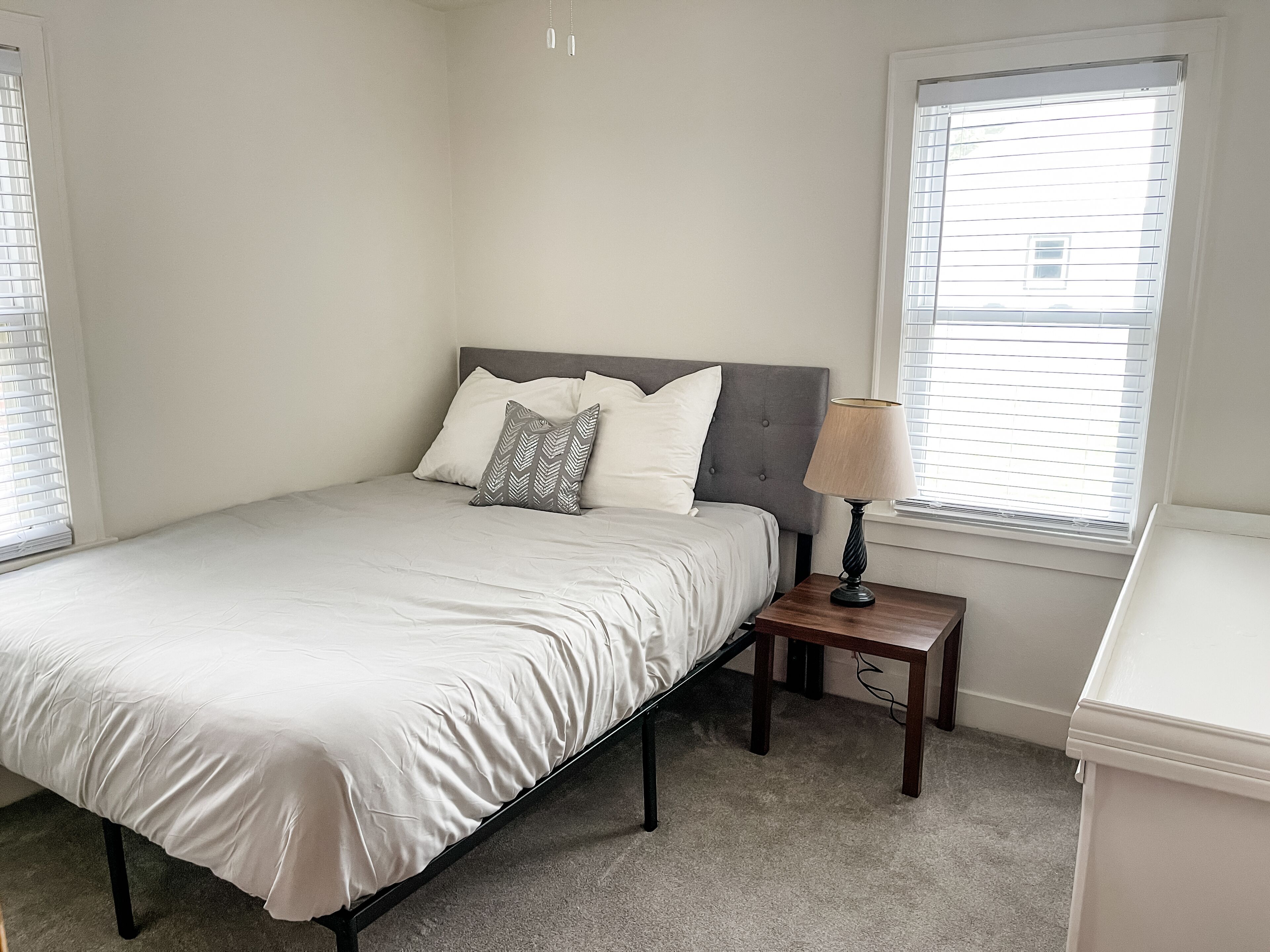 A bedroom with a bed, a nightstand, a lamp, and a window with blinds.