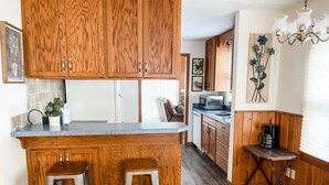 Une cuisine avec des meubles en bois, un îlot central doté de tabourets, un four à micro-ondes et une machine à café.