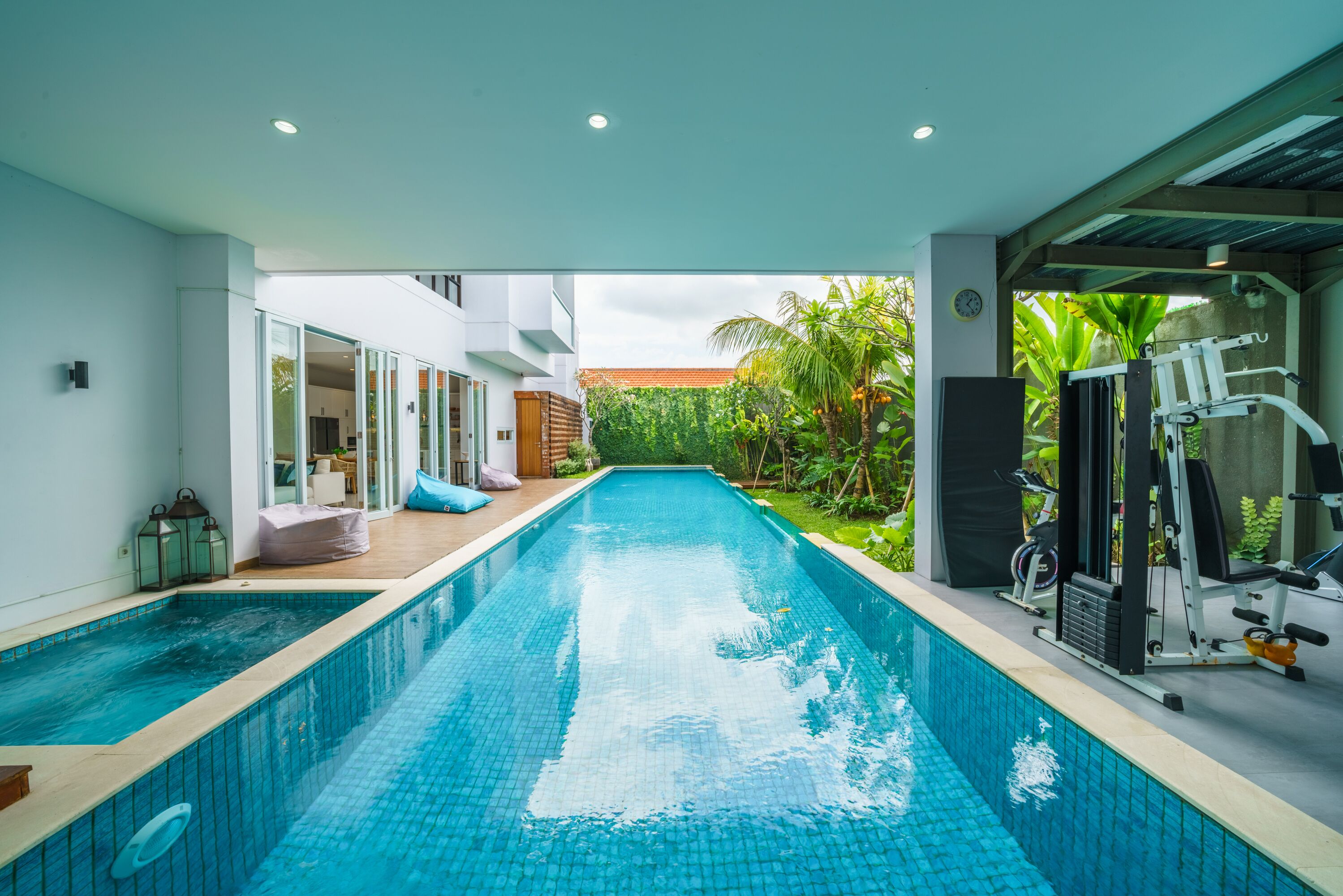 A swimming pool with exercise equipment on one side and a covered area with seating on the other.