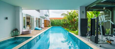 A swimming pool with exercise equipment on one side and a covered area with seating on the other.