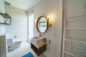 Un baño moderno con lavamanos independiente, espejo redondo con apliques de pared y salpicadero de azulejos blancos.