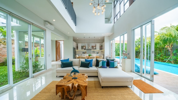 A modern living room with a large sectional sofa, a wooden coffee table, and a view of a swimming pool. - Villa Ammanya (Canggu)