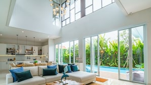 A spacious living room with a large sofa, a coffee table, and a view of a swimming pool through large windows. - Villa Ammanya (Canggu)