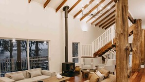 A spacious living room with a large sectional sofa, a wooden coffee table, and a fireplace. There is a staircase with a wooden railing leading to an upper level. - Ampersand Estates (Peerabeelup)
