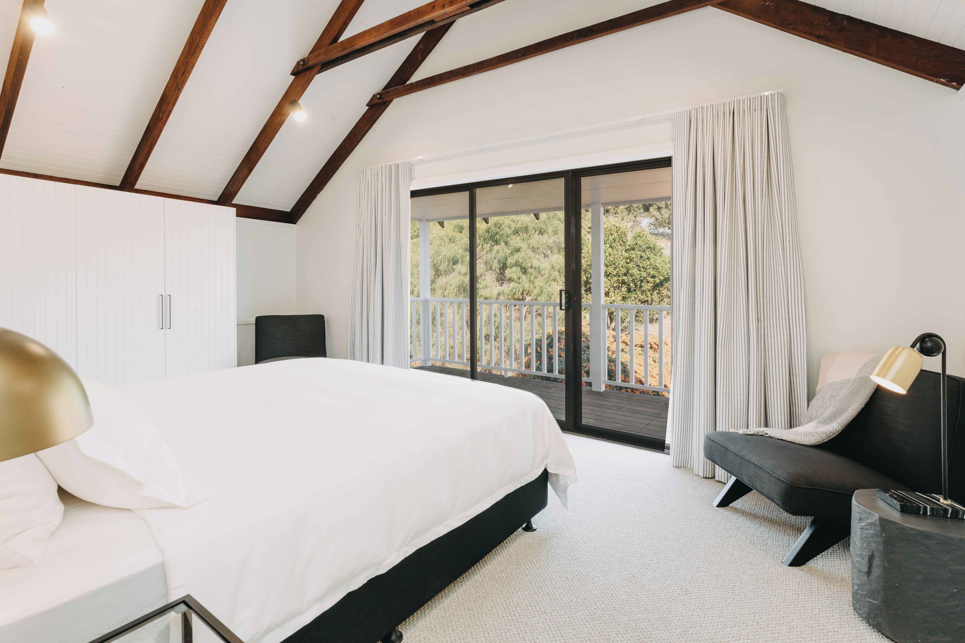 Un dormitorio con una cama grande, un sofá oscuro, una mesita y un balcón con cortinas.