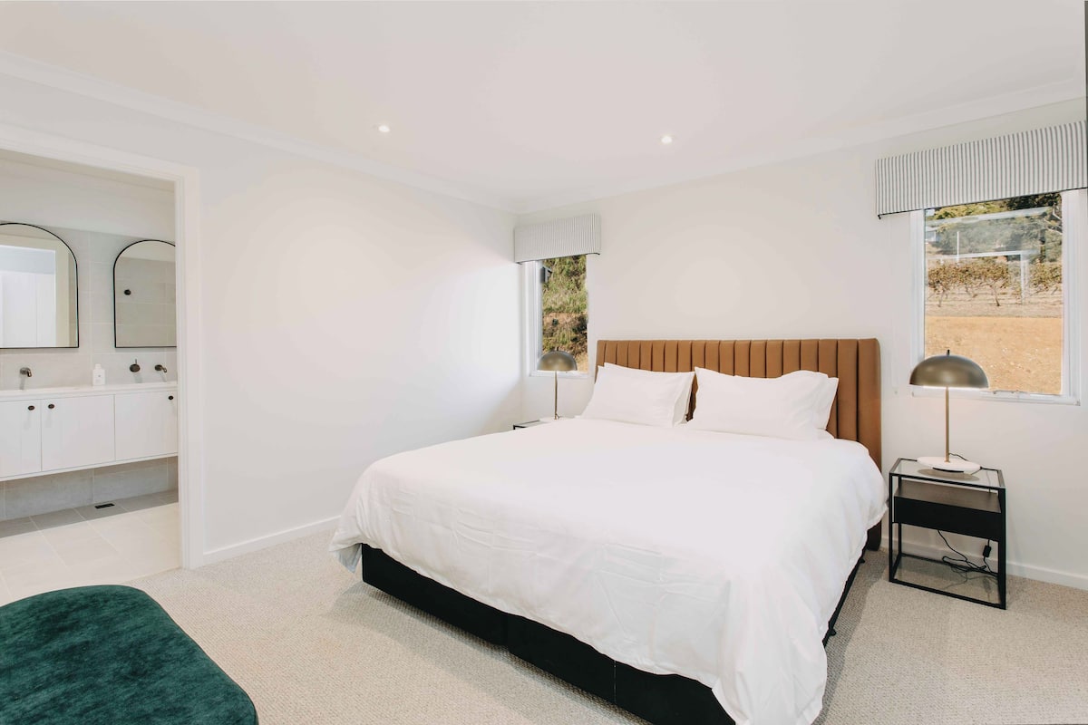 Un dormitorio moderno con una cama grande, un tocador con espejo y una ventana con vistas al exterior.