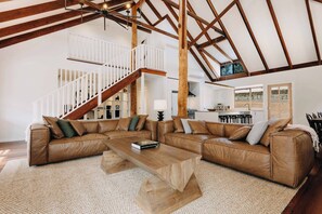 A spacious living area with a large L-shaped brown leather sofa, a wooden coffee table, and a white staircase with a railing.